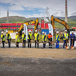 Foto: Aurubis: Viele Menschen mit Helm und Neon-Veste stehen in einer Reihe auf einer Baustelle mit jeweils einer Schaufel in der Hand